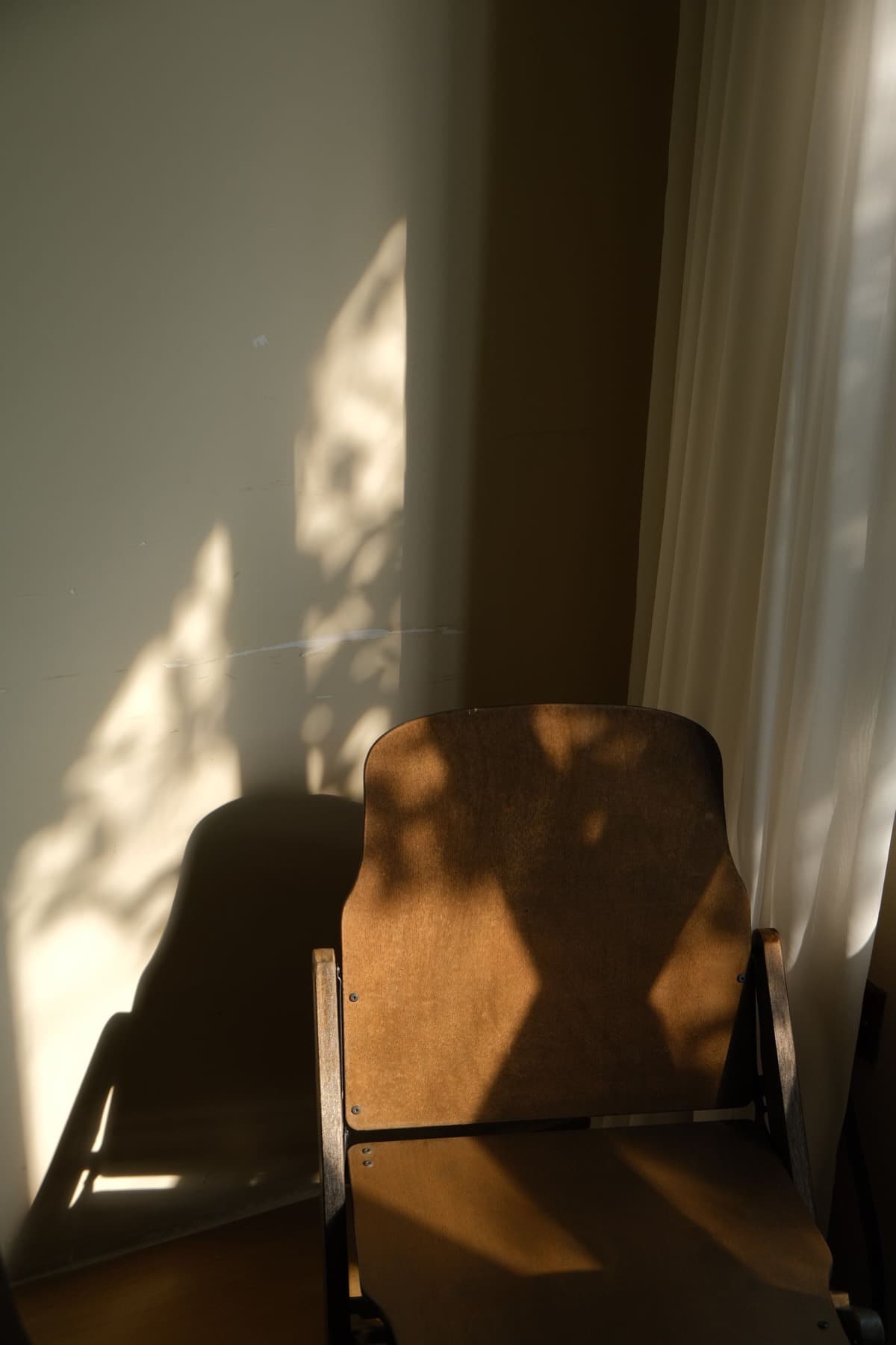 A wooden chair in afternoon light beside a curtain.